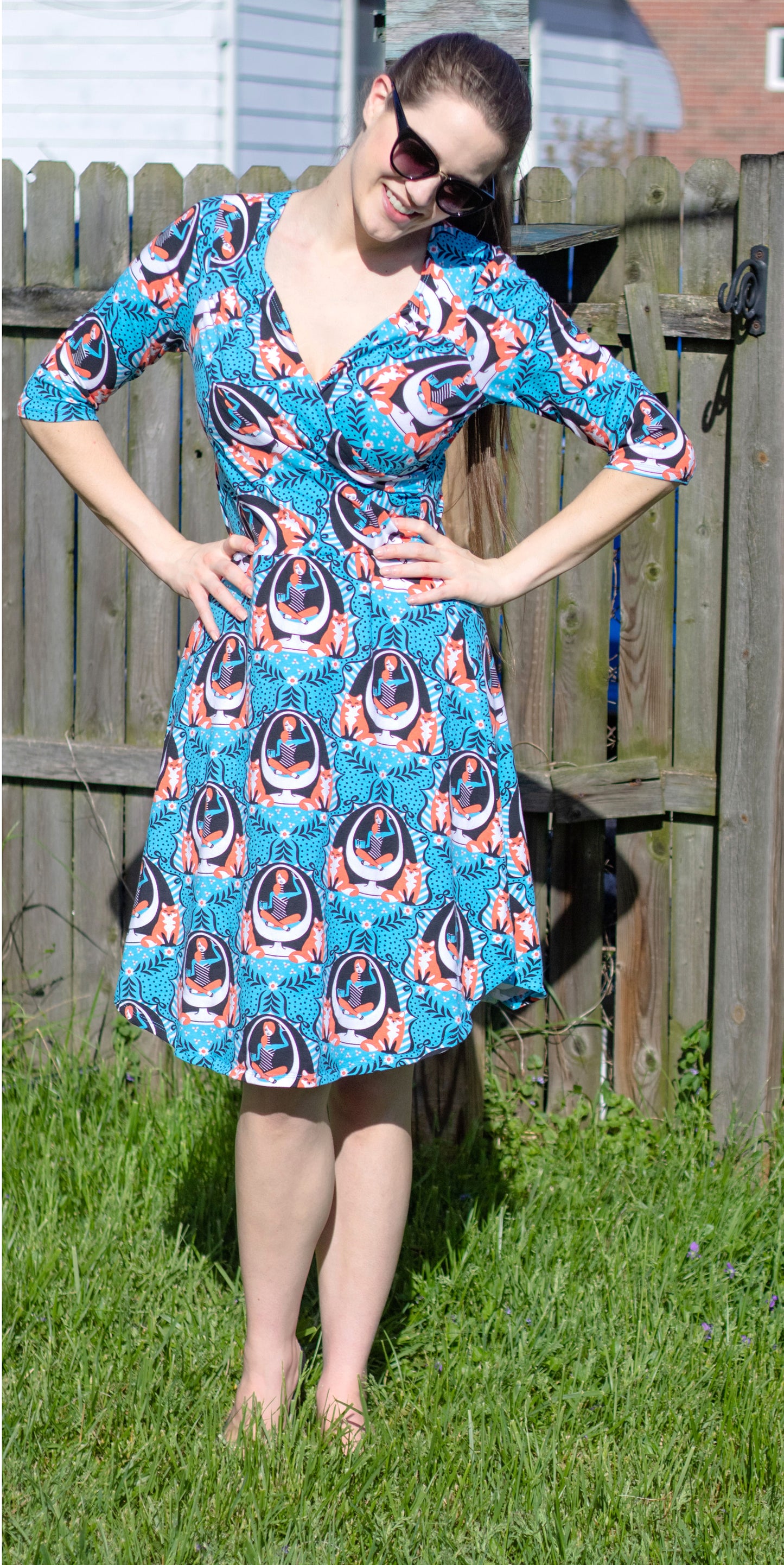 Model in blue sleeved wrap dress featuring print of foxes and girls reading books sitting in an egg chair