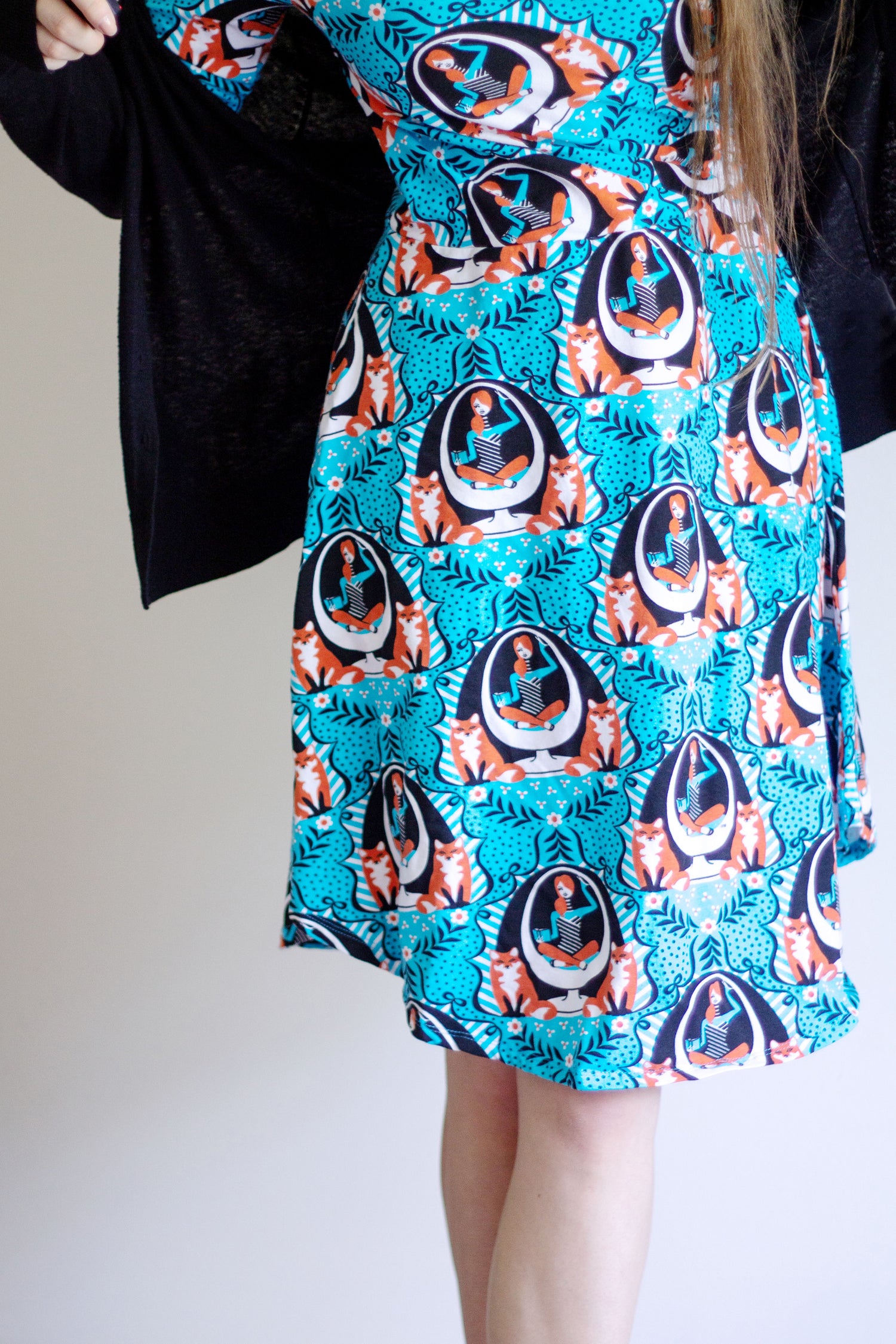 Closeup of skirt of wrap dress featuring blue and orange print of foxes and girls reading books in an egg chair
