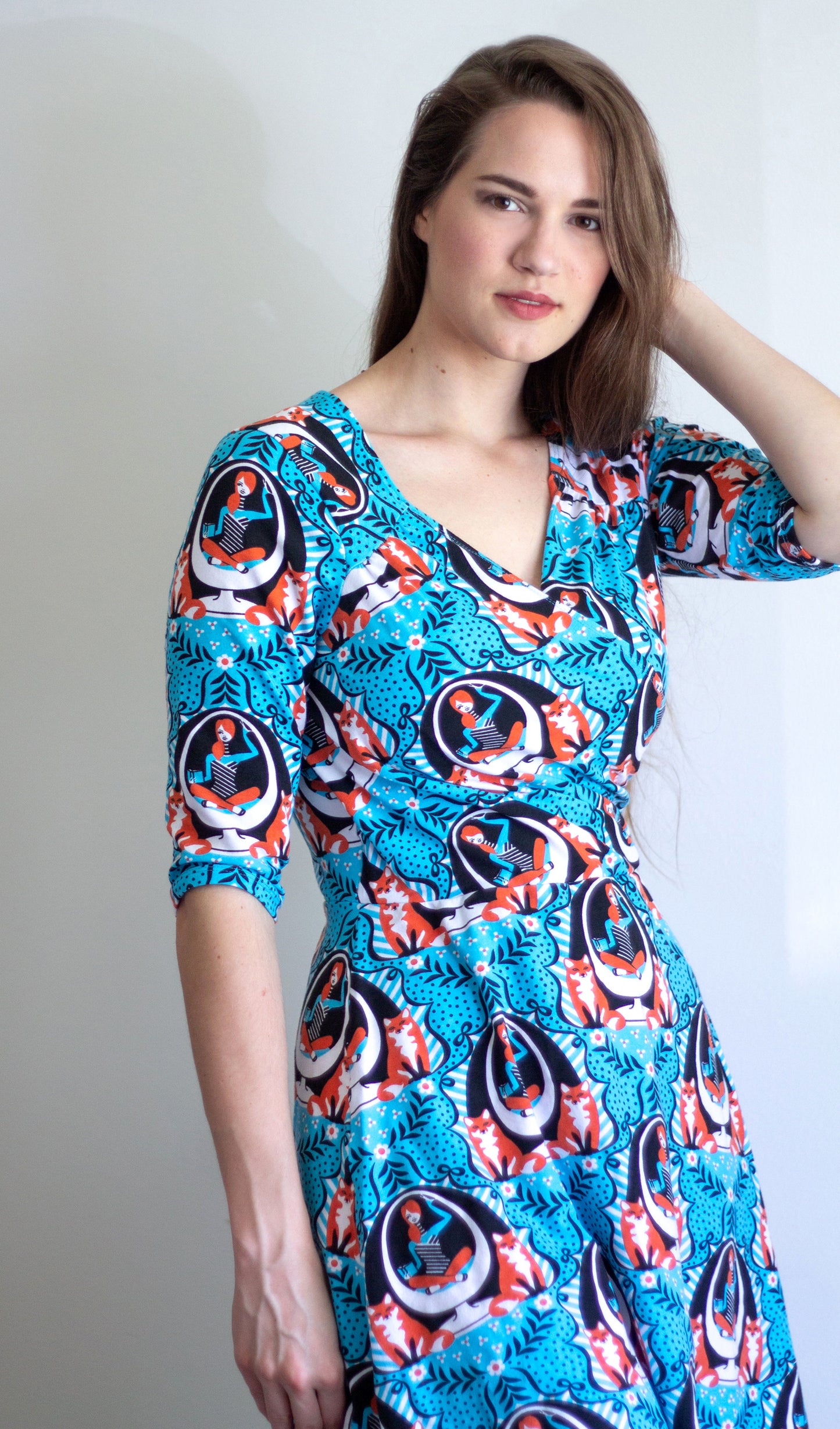 Closeup of model in blue sleeved wrap dress featuring print of foxes and girls reading books in an egg chair