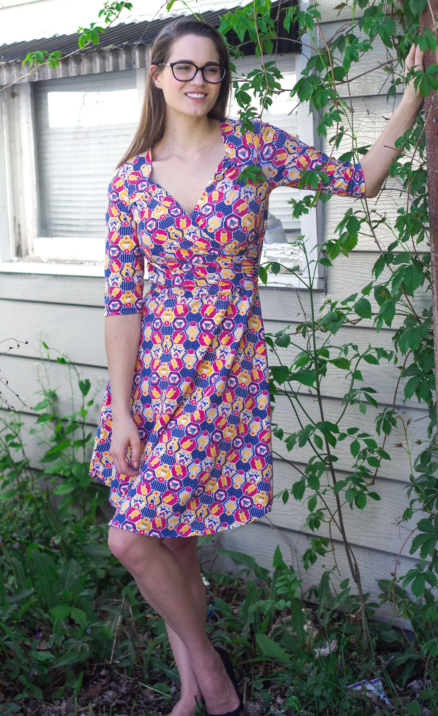 Red, yellow and blue honeycomb and honeybee print sleeved knee-length wrap dress on model standing outside