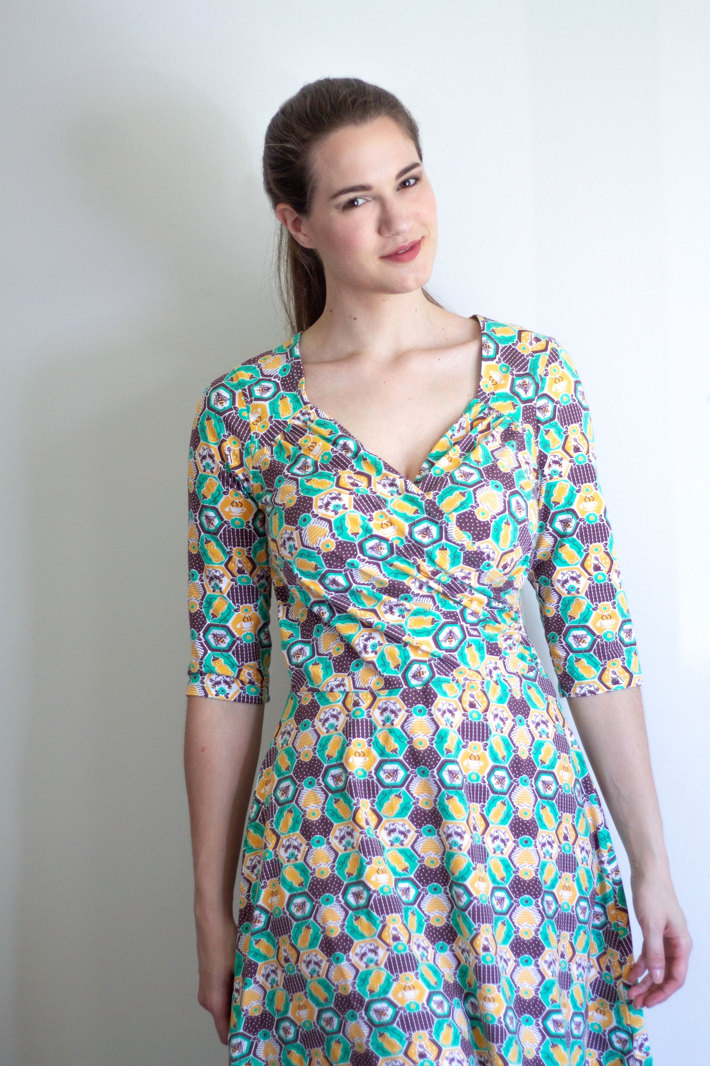 Closeup of brown-haired model wearing yellow, green and brown honeybee and hexagon print wrap dress
