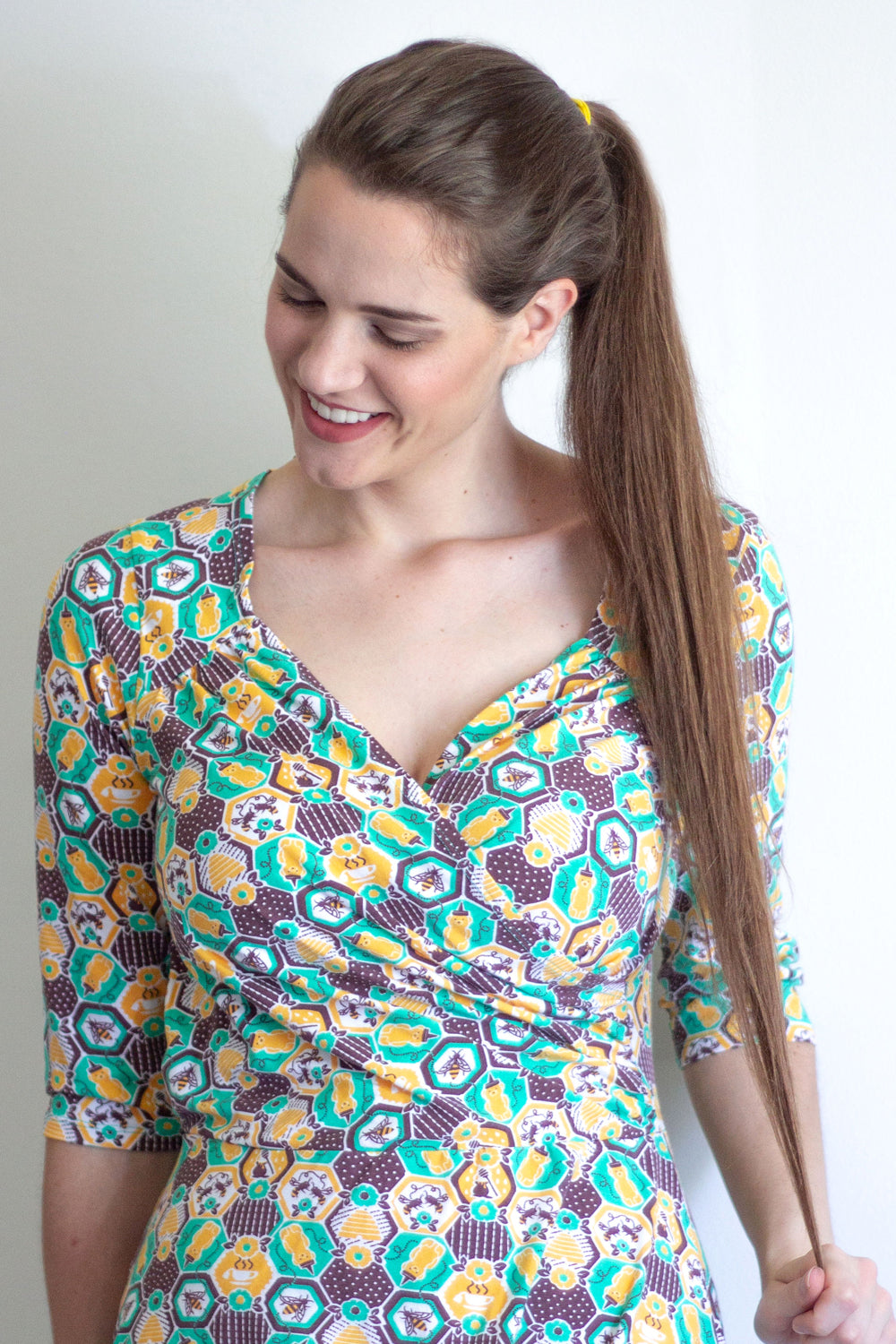 Brown-haired model wearing yellow, green and brown honeybee and hexagon print wrap dress