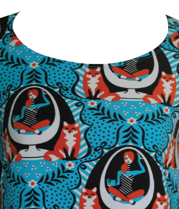 Closeup of bright blue tunic with print of foxes and girls reading books sitting in an egg chair