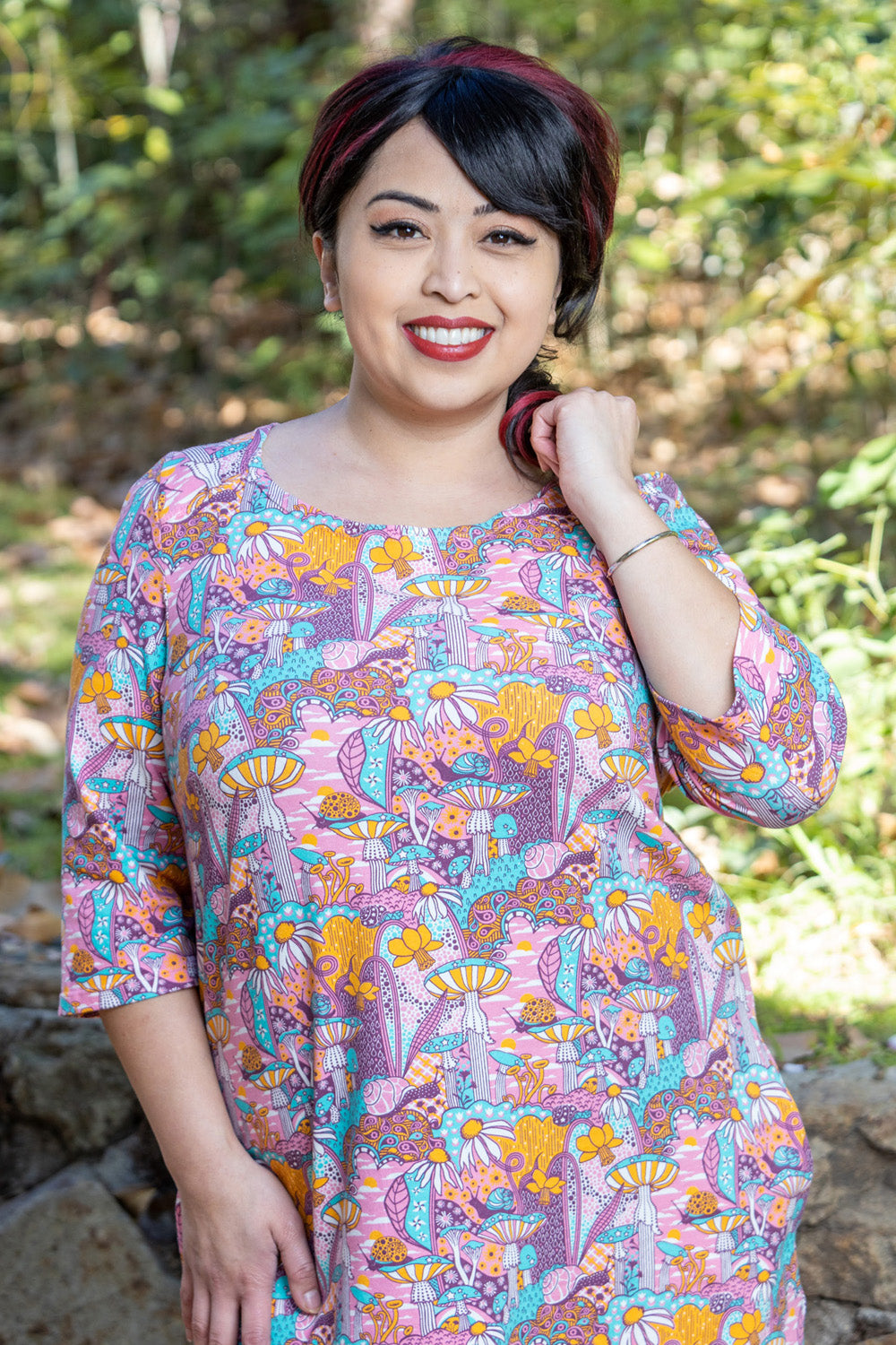 Model wearing pink, yellow and aqua pocket tunic with mushrooms, flowers and snails