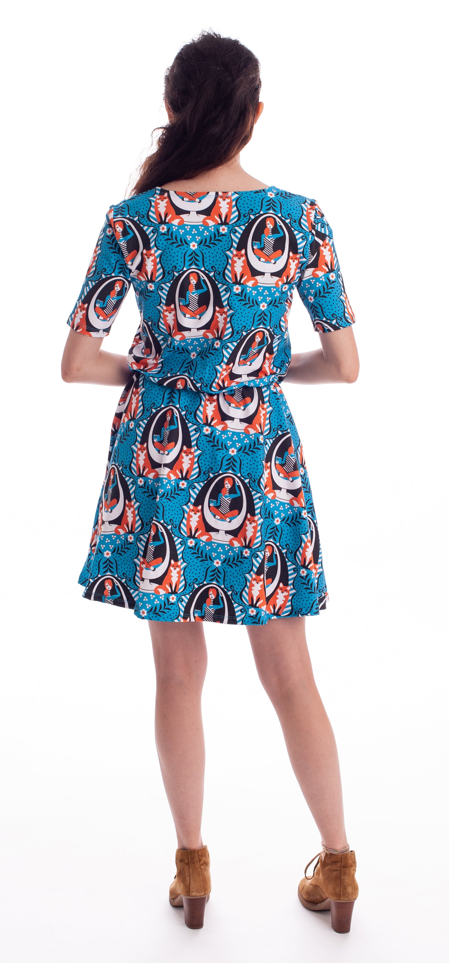Dark haired model wearing bright blue dres with graphic of redhead girl sitting in egg chair flanked by two foxes