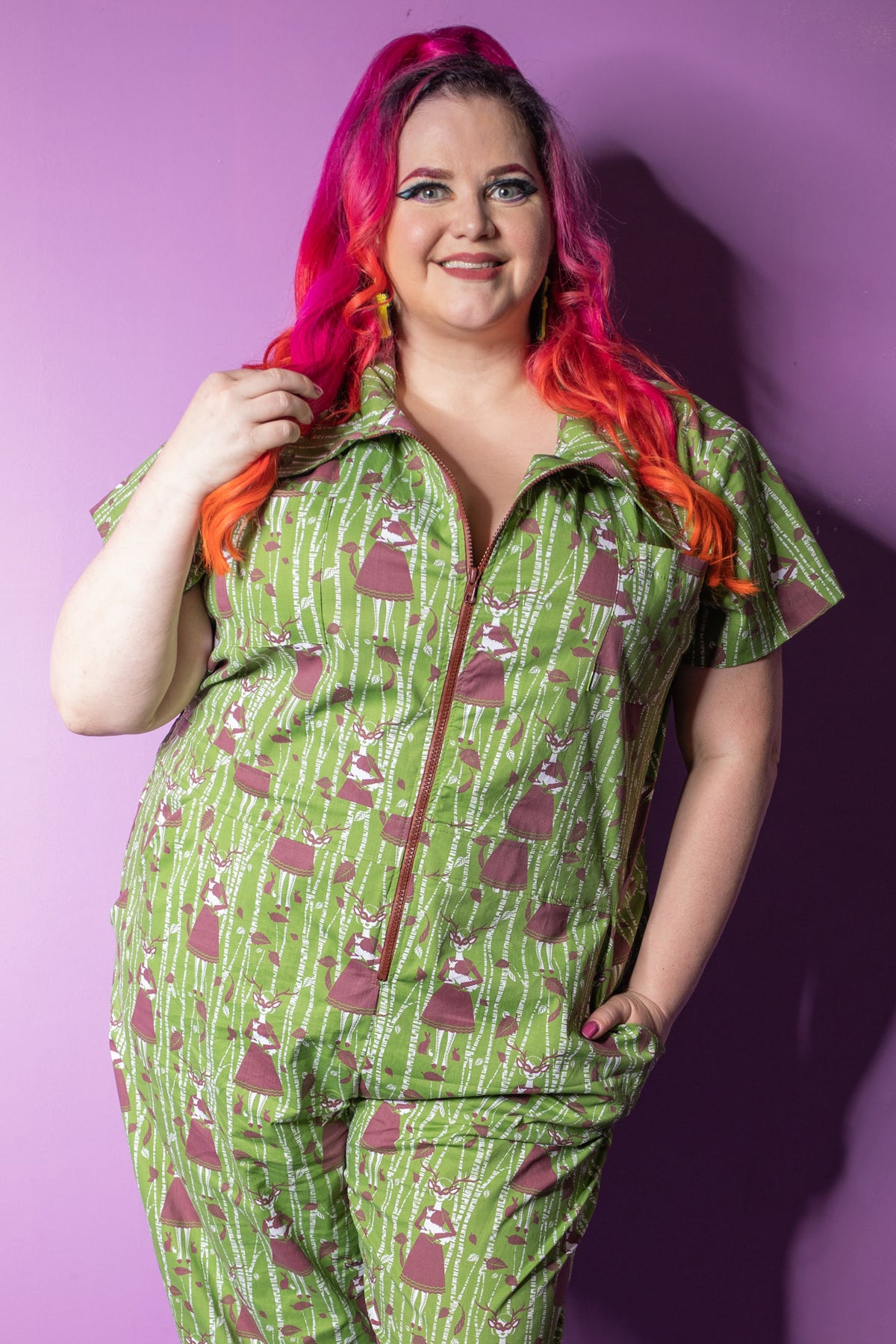 Pink-haired model in green and brown deer and trees jumpsuit with big zipper and several pockets