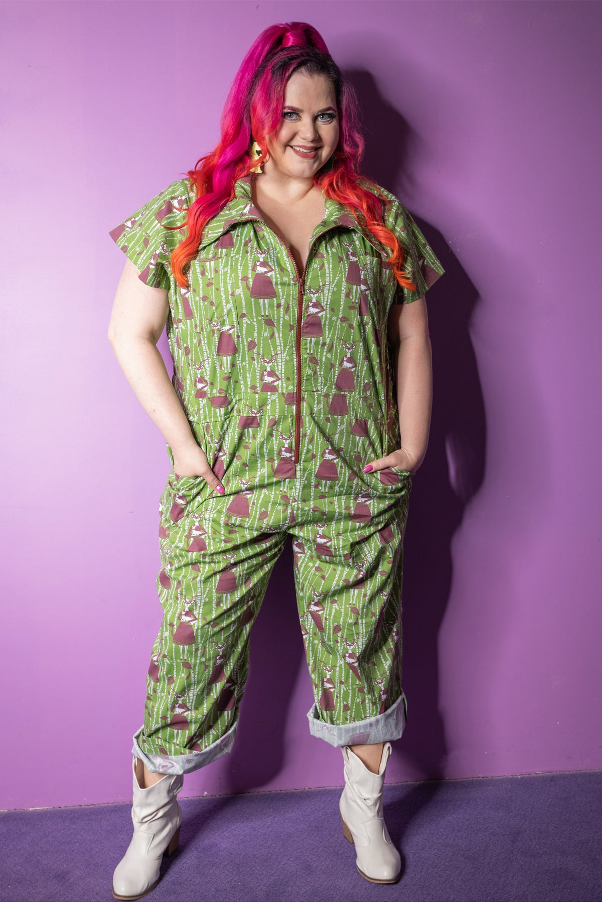 Pink-haired model in green and brown deer and trees jumpsuit with big zipper and several pockets