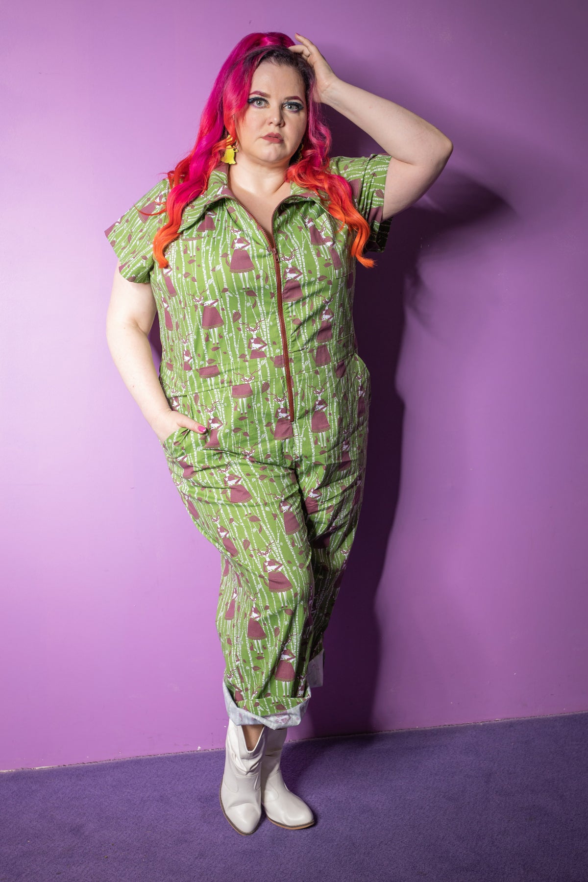Pink-haired model in green and brown deer and tree print jumpsuits with big zippers and pockets