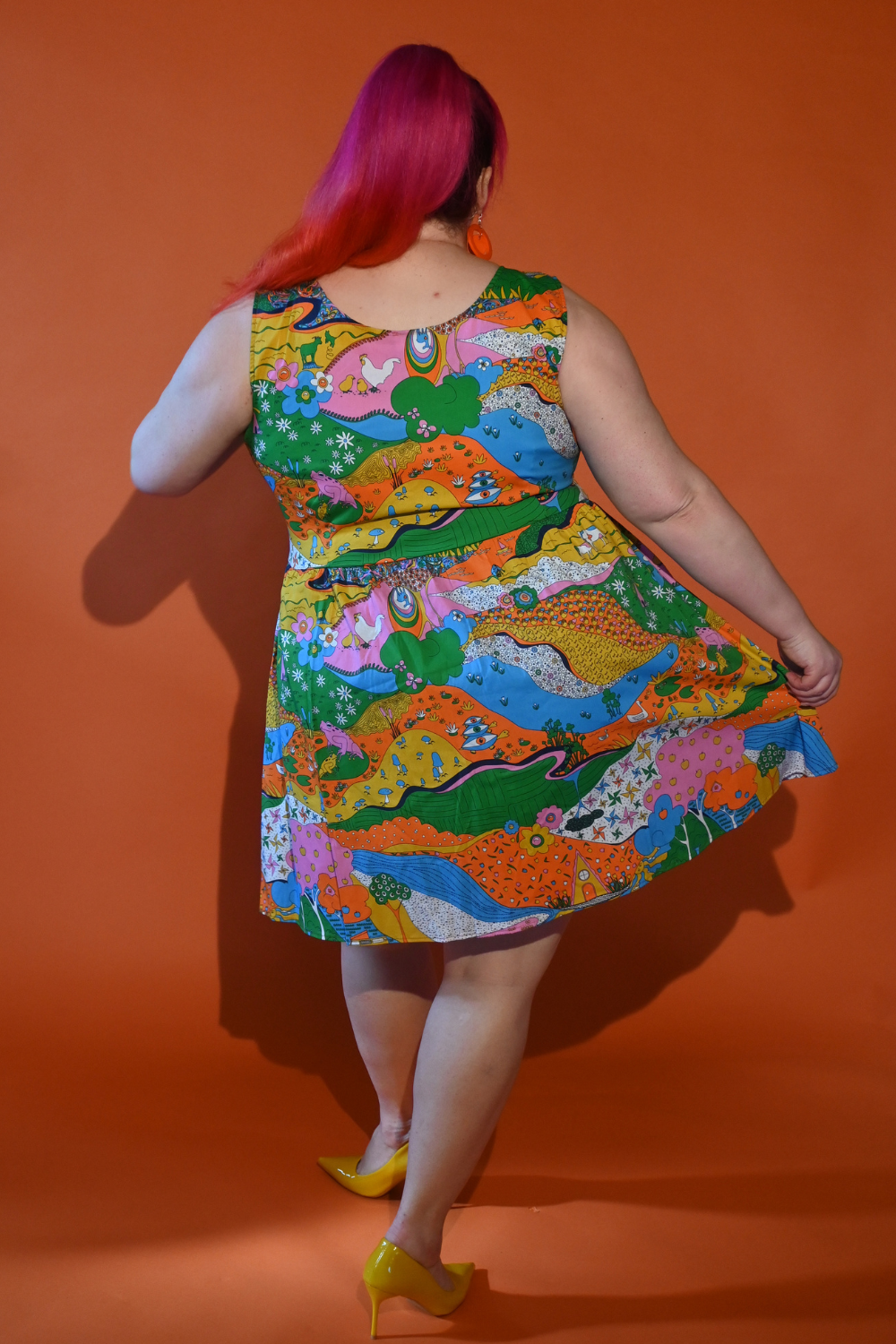 Back view of pink-haired girl in rainbow colored landscape print fit & flare dress