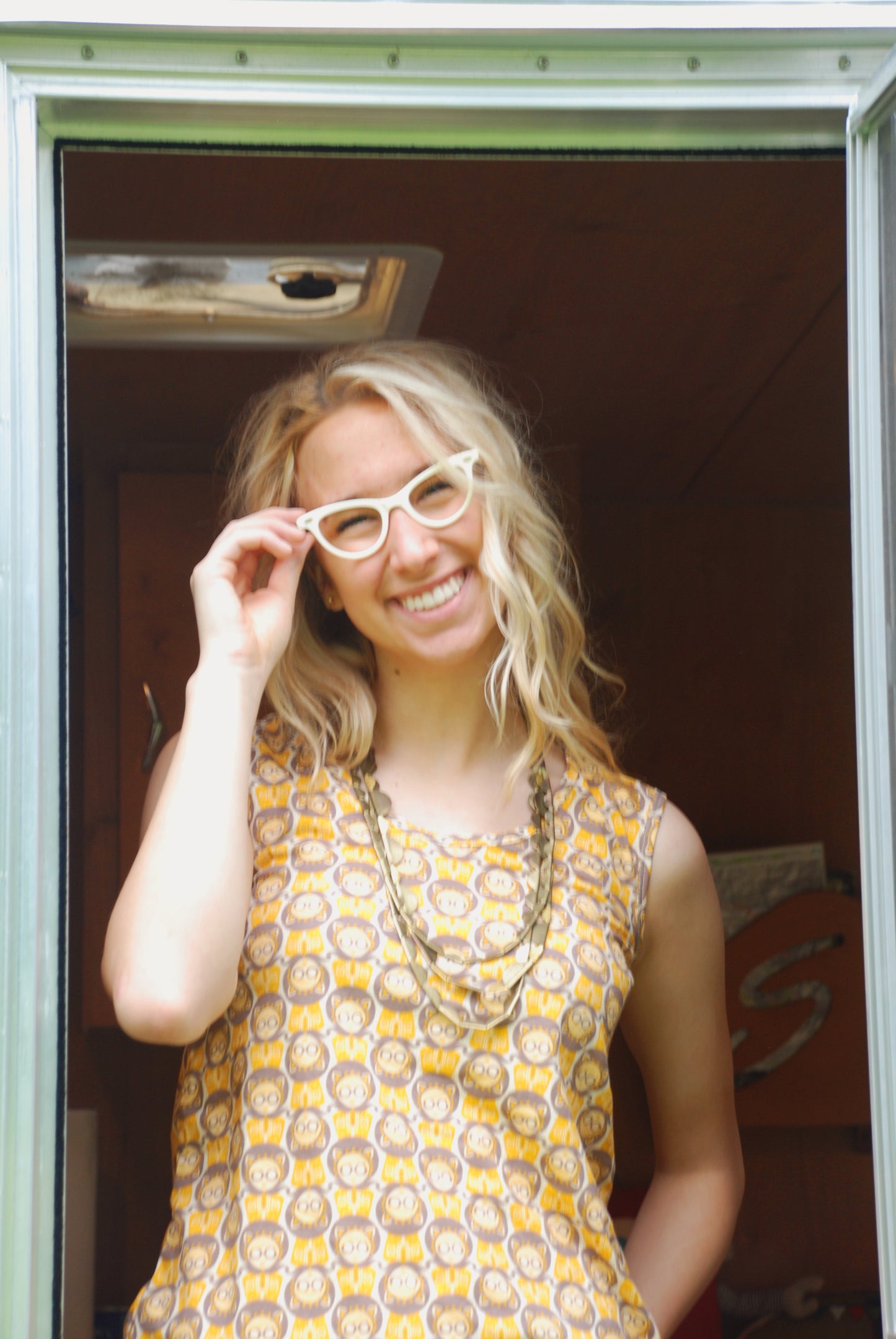 Closeup of girl standing in the doorway of a camper & wearing glasses and a sleeveless grey and yellow tee