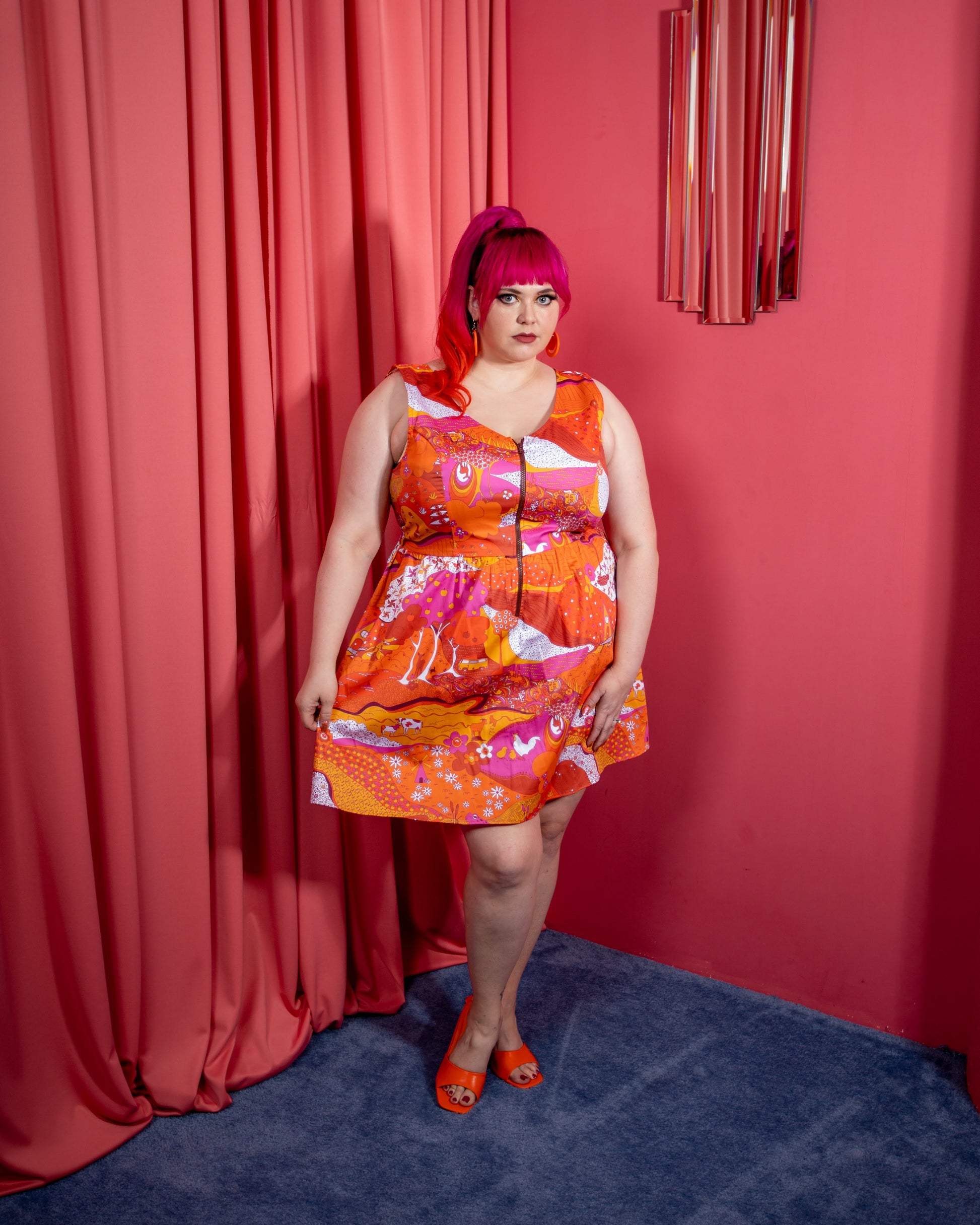 Pretty pink-haired model in bright red orange and pink dress with front zip in pink room