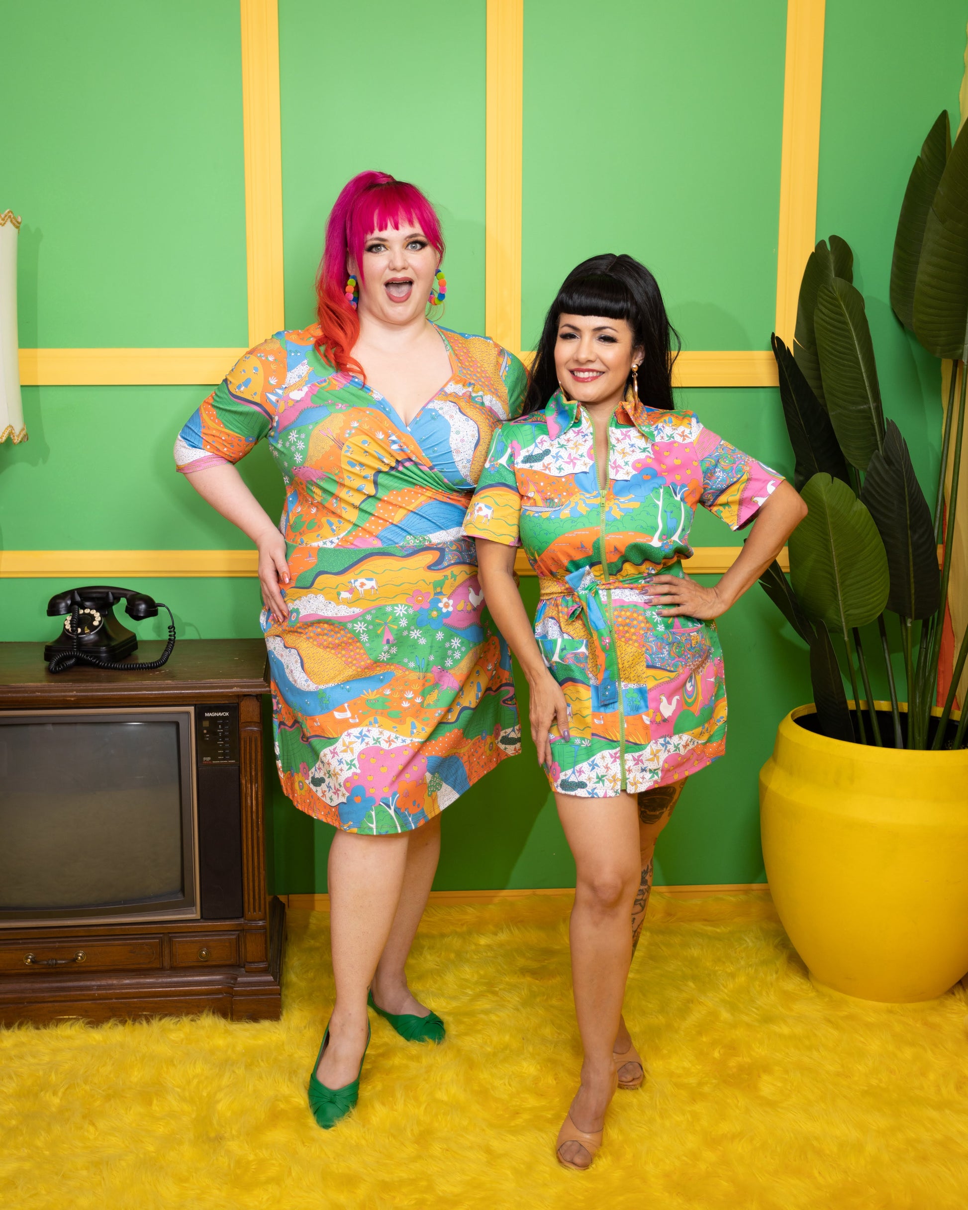 2 pretty models wearing bright rainbow landscape print dresses with chickens, trees, turtles, rivers and other fun elements