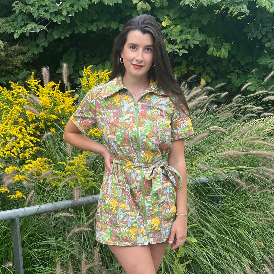 Dark-haired model in olive green, rust and mustard belted zip-front collared minidress outside in nature