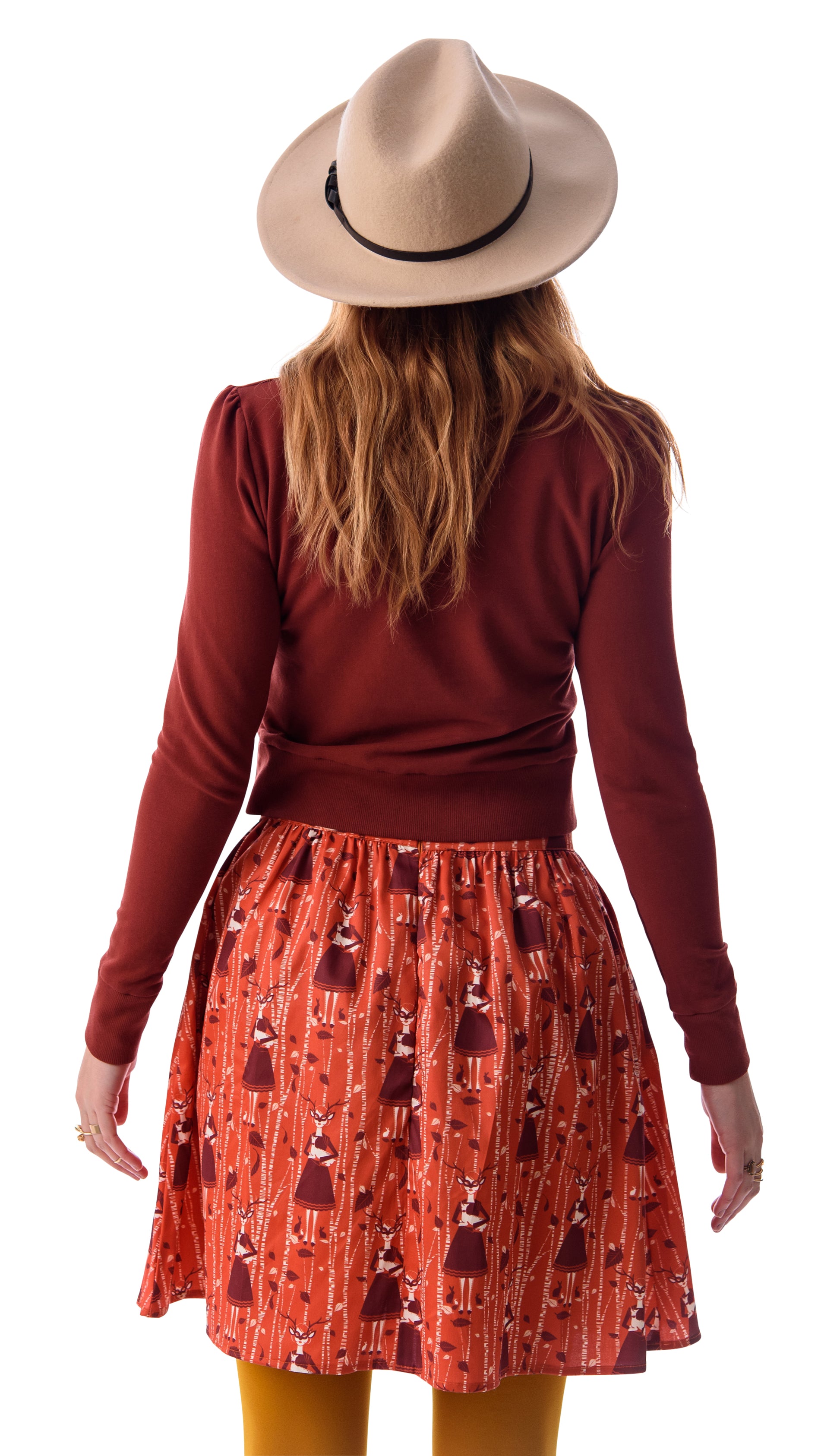 Back view of orange and brown skirt with deer, birches and masked girl print and pockets