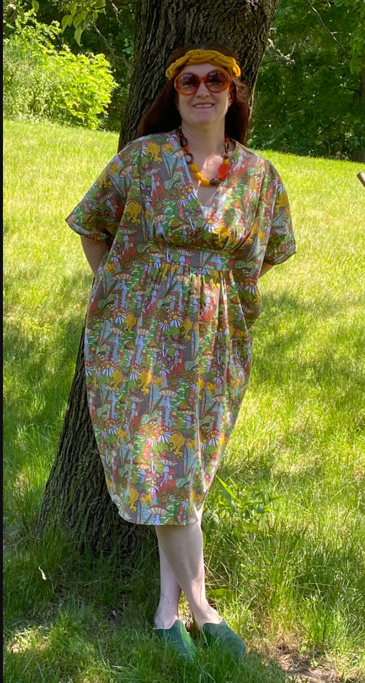 Smiling girl wearing v-neck olive green, yellow, and orange mushroom, floral and snail print midi caftan
