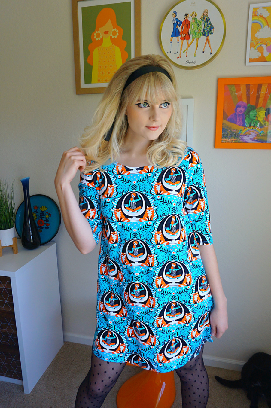 Bright blue pocket tunic featuring print of foxes and girls reading books sitting in an egg chair