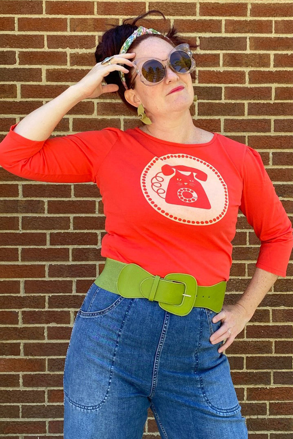 Bright red 3/4 sleeve graphic tee with rotary dial cat phone print surrounded by a circle, on woman in sunglasses