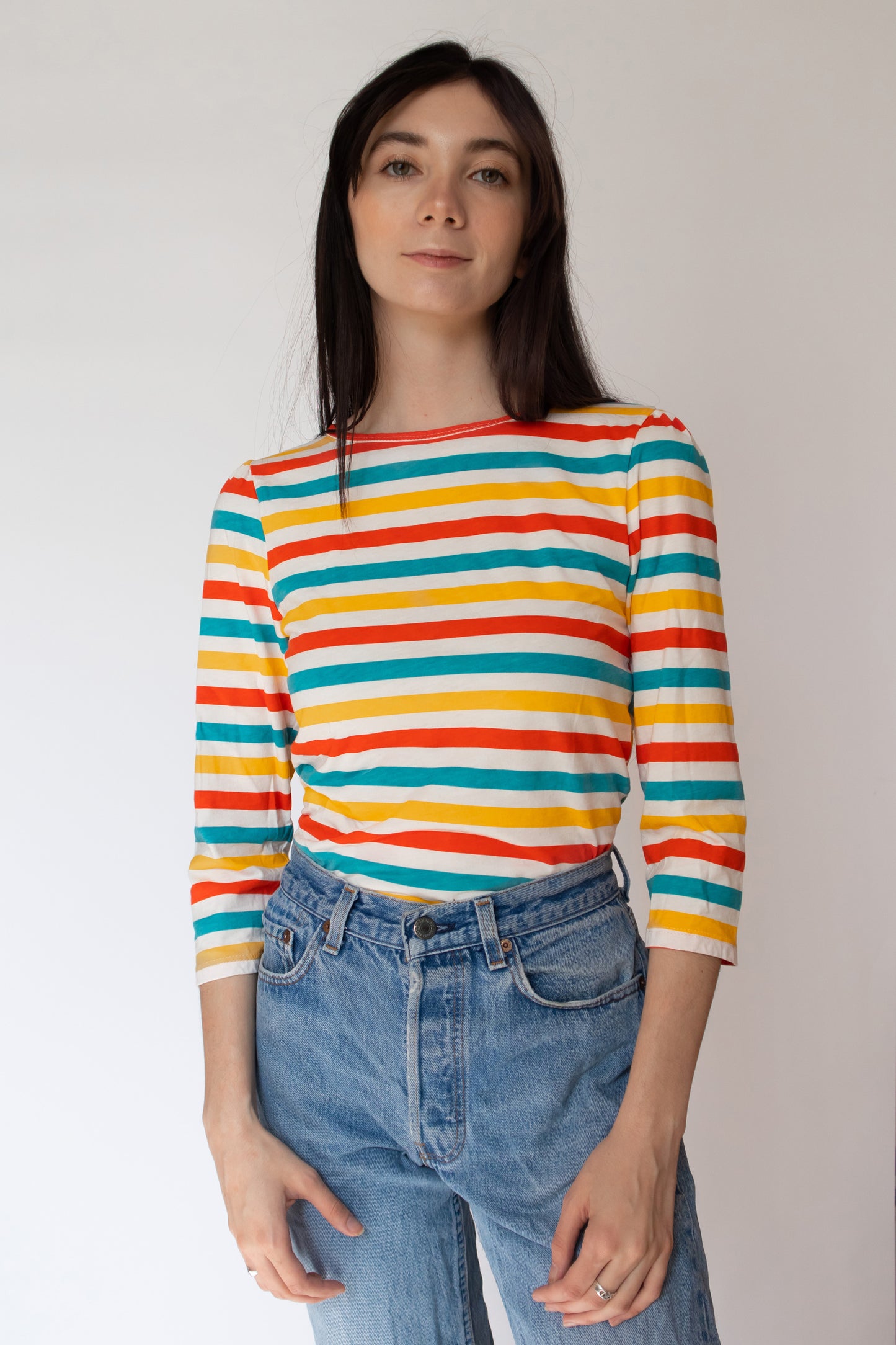 Dark-haired model in bright orange, yellow and blue 3/4 sleeved striped shirt 