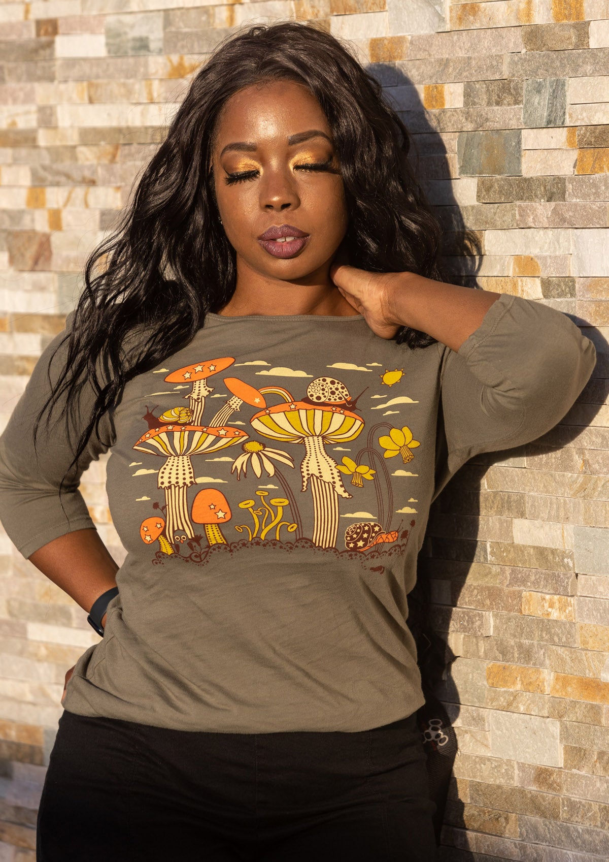 Long-haired model in olive green 3/4 sleeve tee with mushrooms, snails and flowers