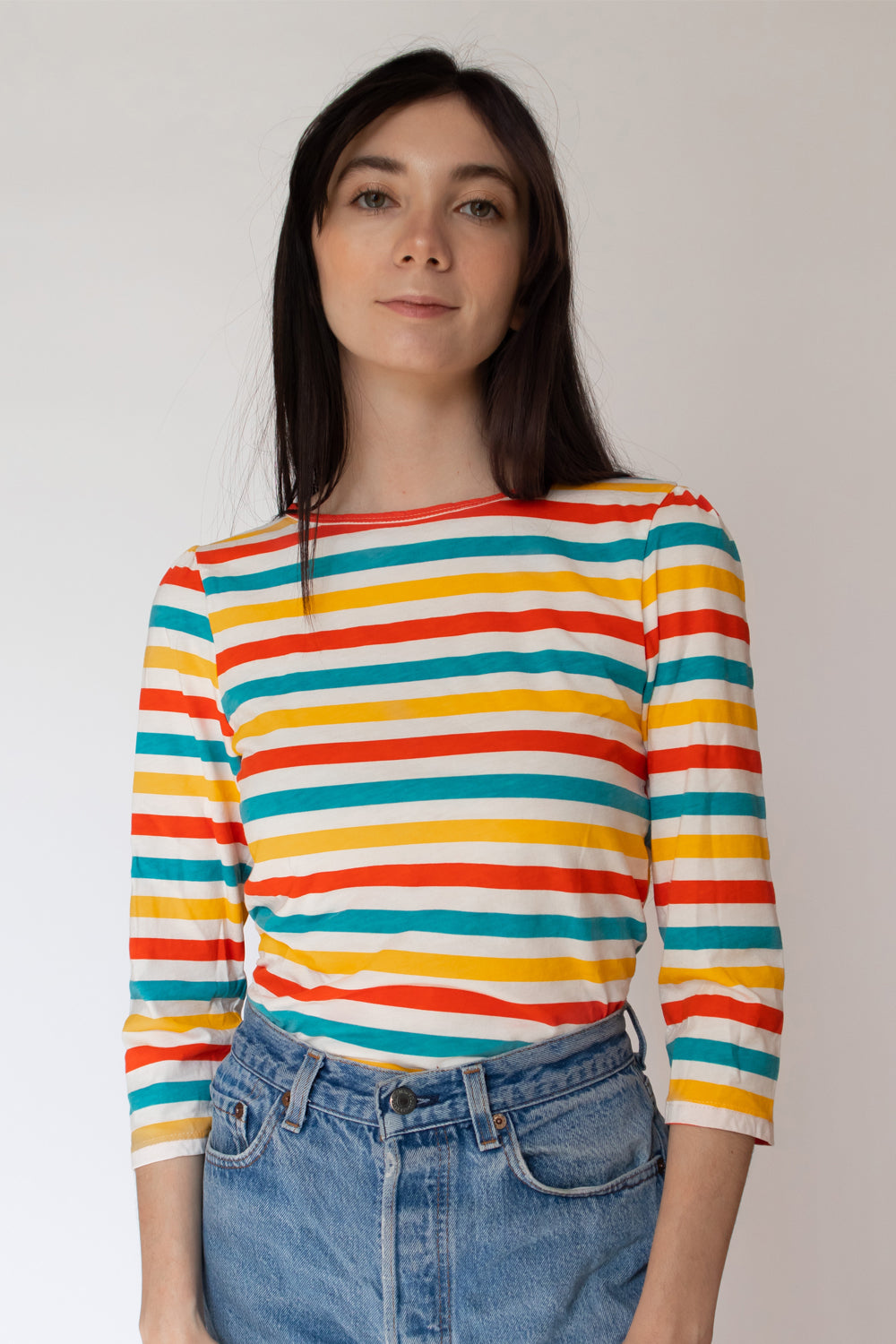 Dark-haired model in bright orange, yellow and blue 3/4 sleeved striped shirt