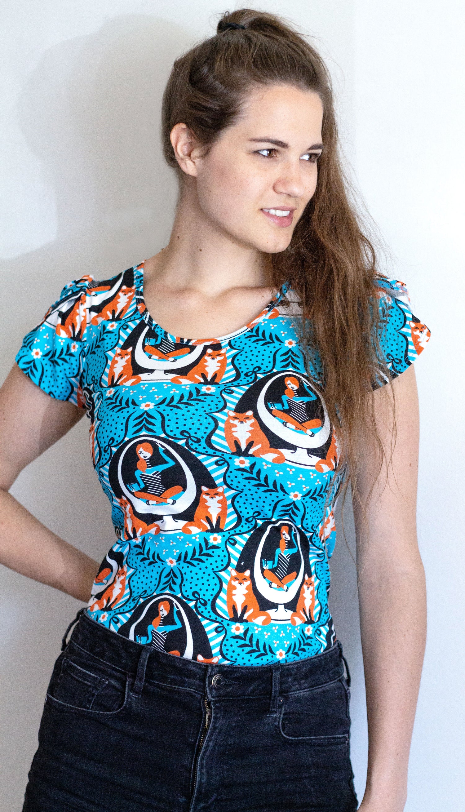 Model in bright blue tulip-sleeve tee with foxes, girl reading in egg chair print in orange, black and white