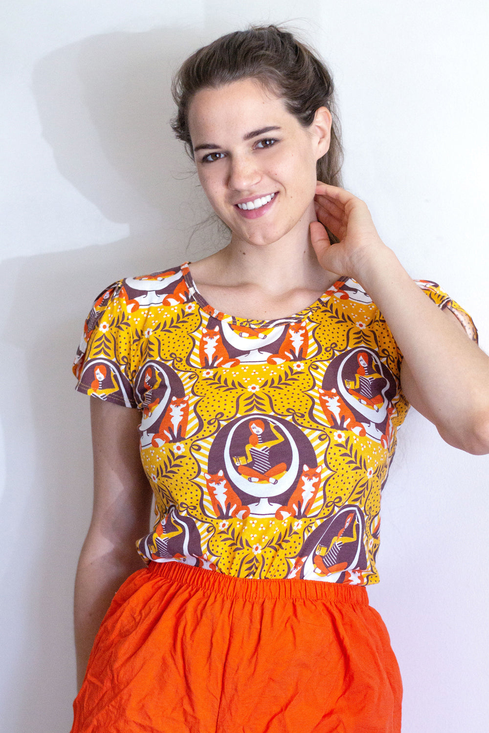 Model in yellow tulip-sleeve tee with foxes, girl reading in egg chair print in orange, brown and white