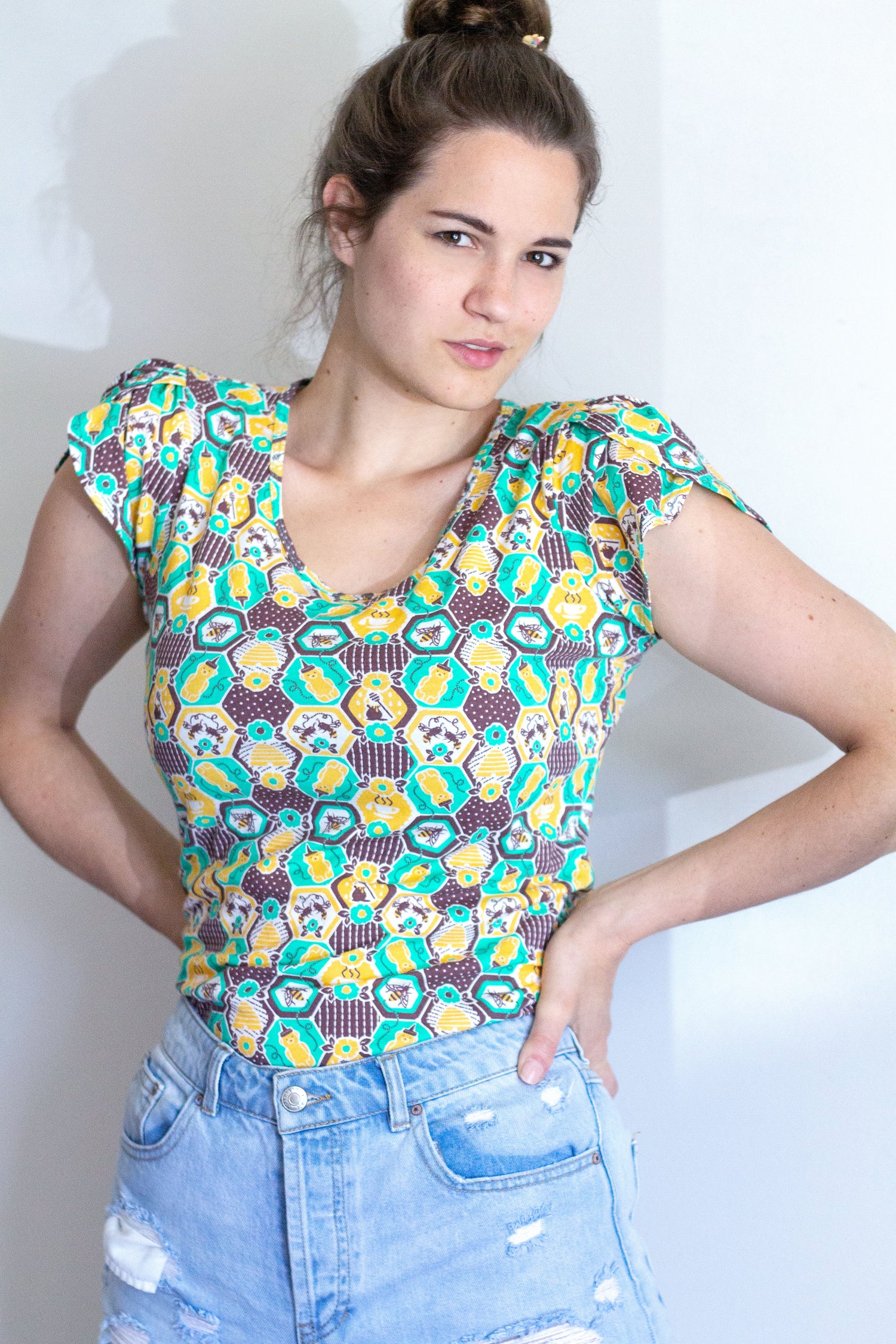Green, yellow and brown honeycomb, bee and flower print tulip-sleeved tee on brown-haired model 