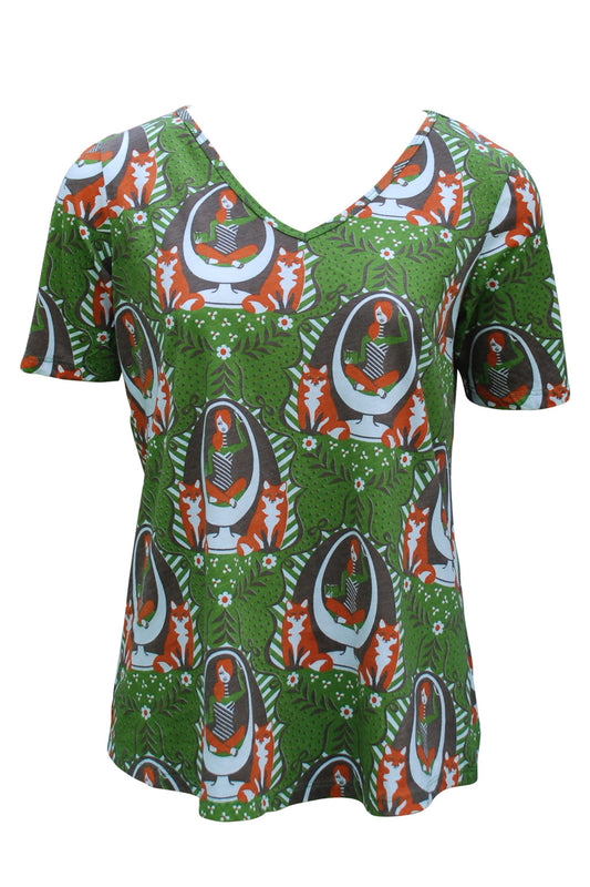 Olive green V neck shirt with brown, orange and white print of girl reading in egg chair and foxes 