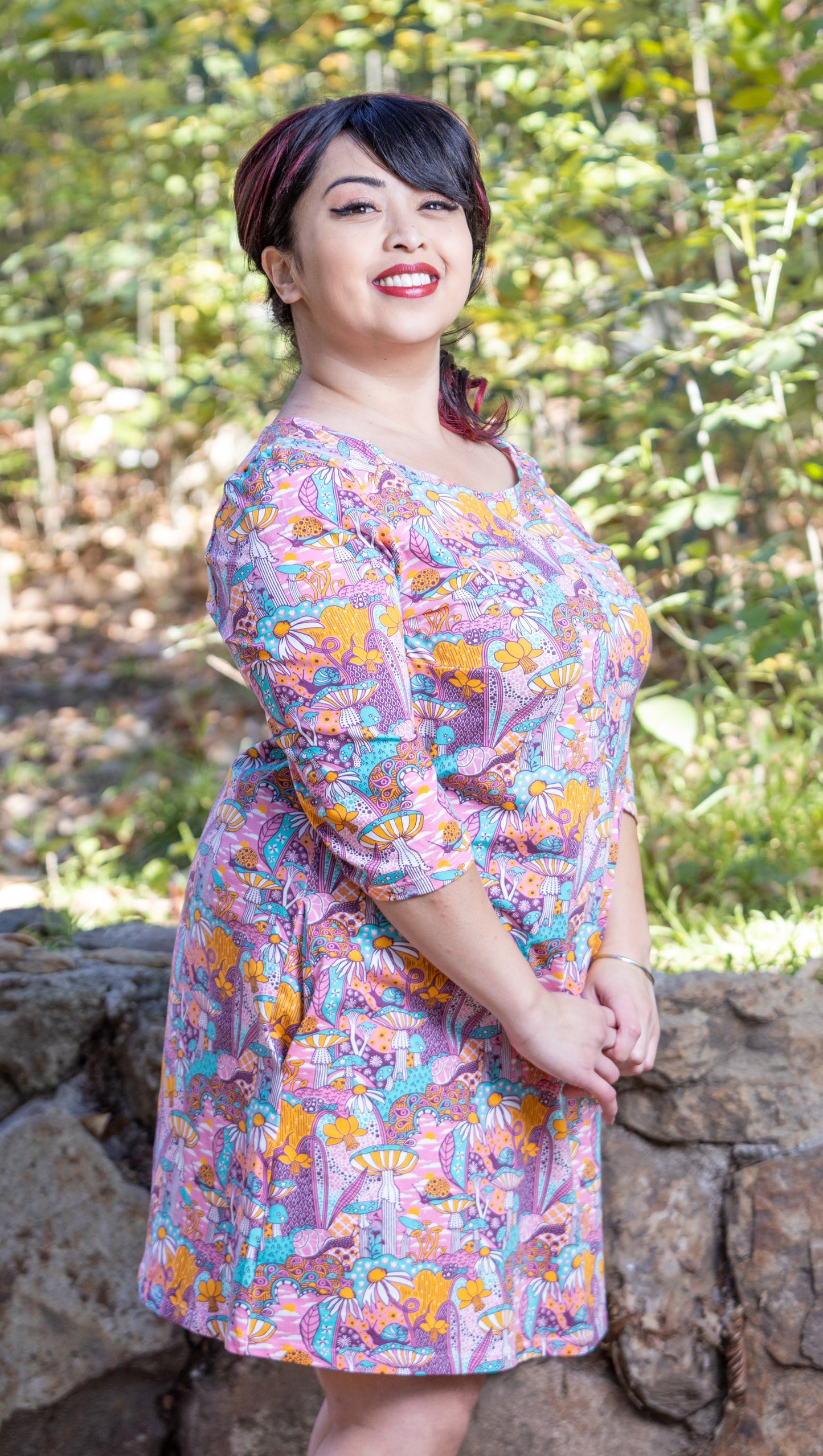 Side view of model wearing pink, yellow and aqua pocket tunic with mushrooms, flowers and snails 