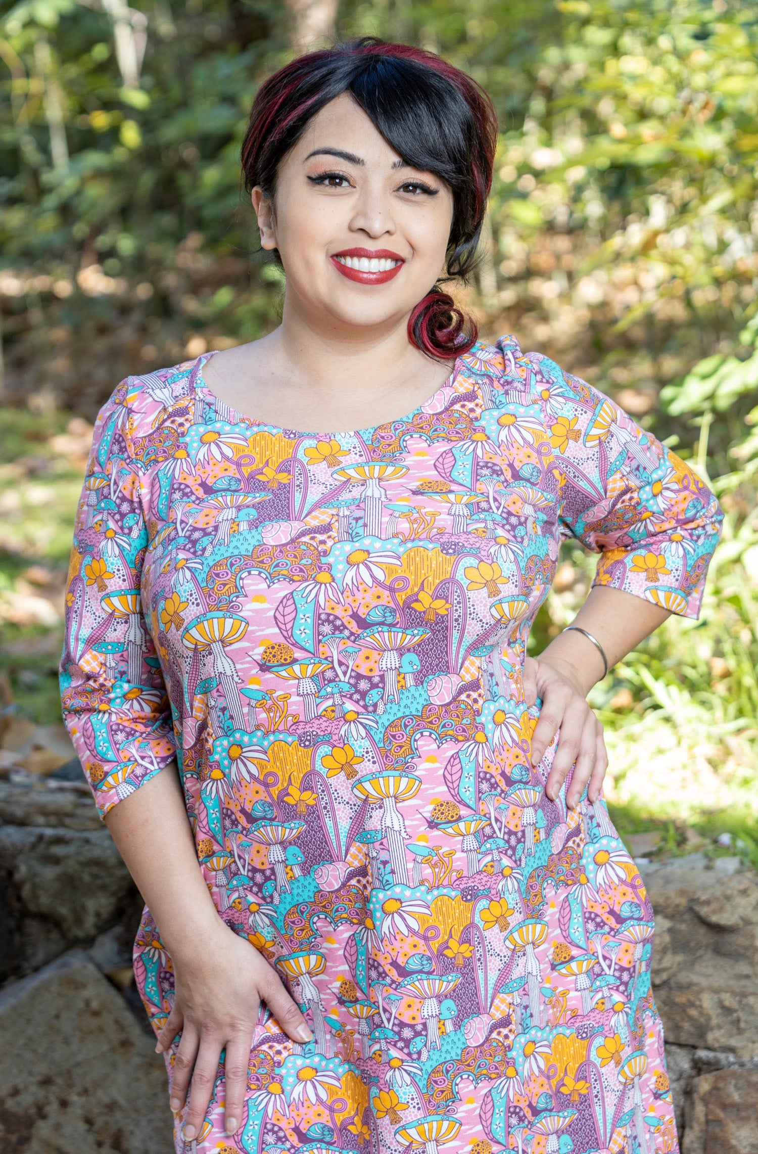 Model wearing pink, yellow and aqua pocket tunic with mushrooms, flowers and snails 