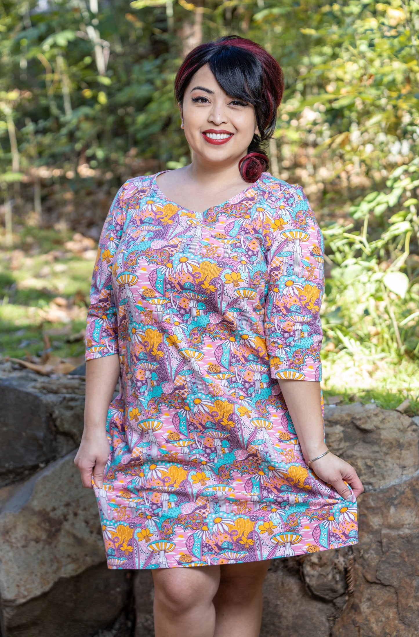 Model wearing pink, yellow and aqua pocket tunic with mushrooms, flowers and snails 