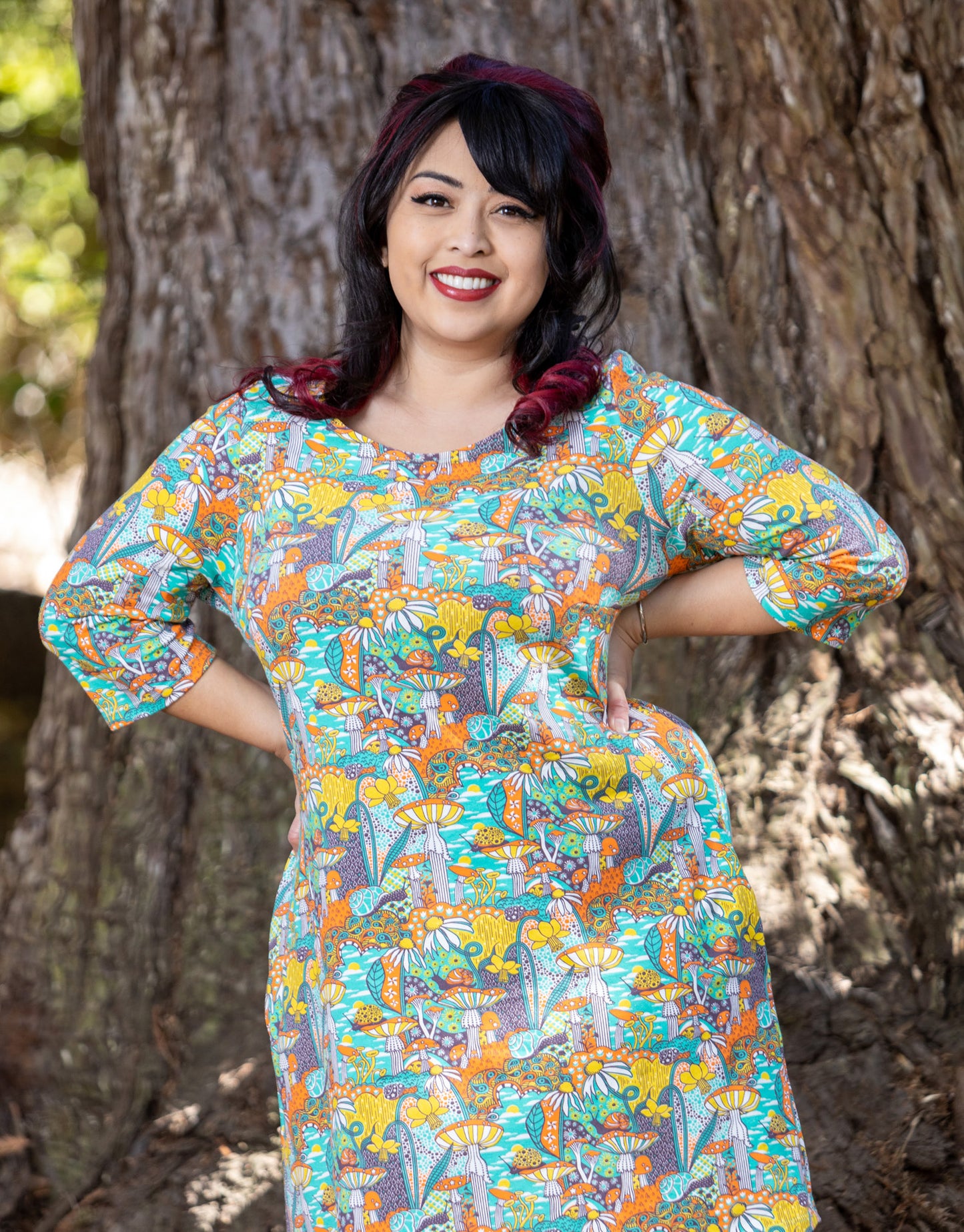 Model wearing teal, orange and yellow  pocket tunic with mushrooms, flowers and snails 