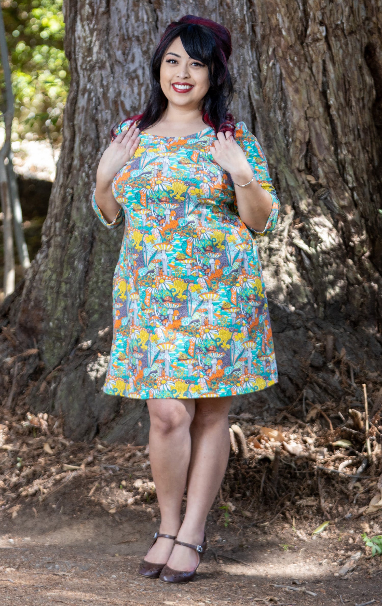Model wearing teal, orange and yellow pocket tunic with mushrooms, flowers and snails