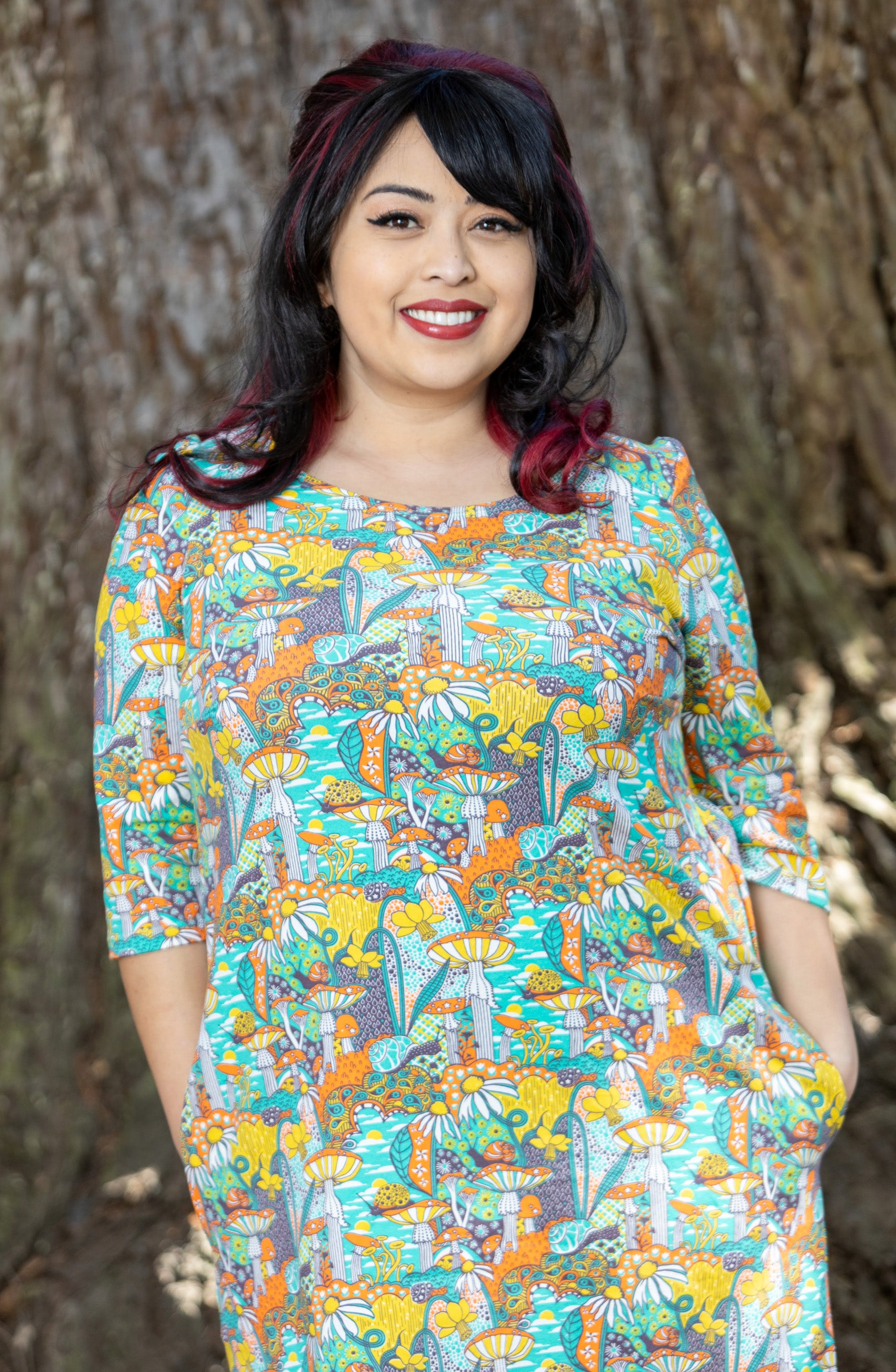 Model wearing teal, orange and yellow pocket tunic with mushrooms, flowers and snails