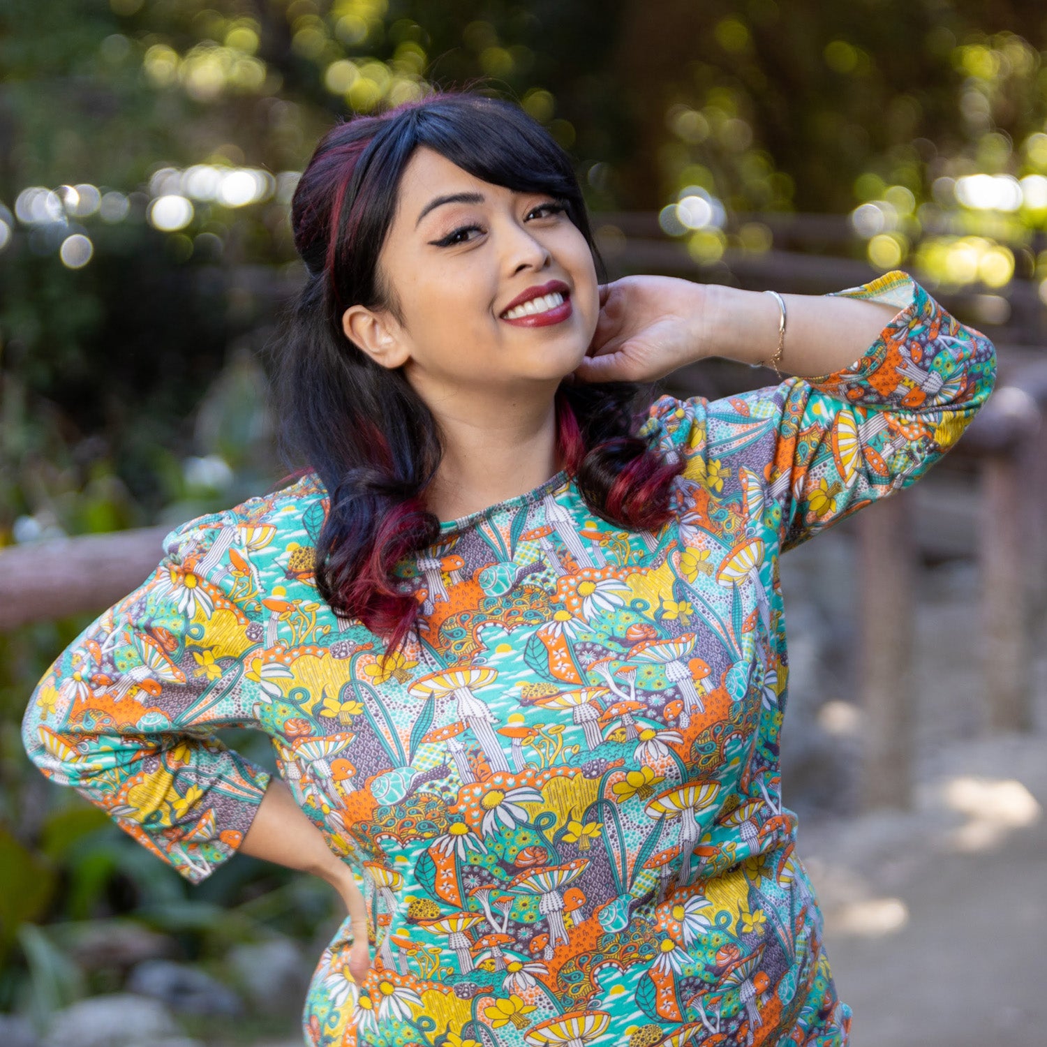 Model wearing 3/4 sleeve shirt featuring colorful fantasy landscape and mushrooms