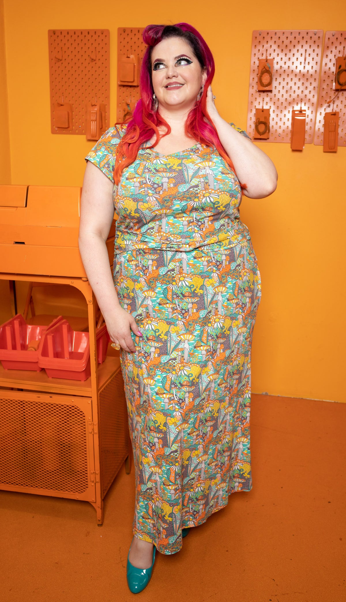 Model wearing twist belt, cap-sleeved dress featuring yellow, orange and green mushrooms, snails and flowers