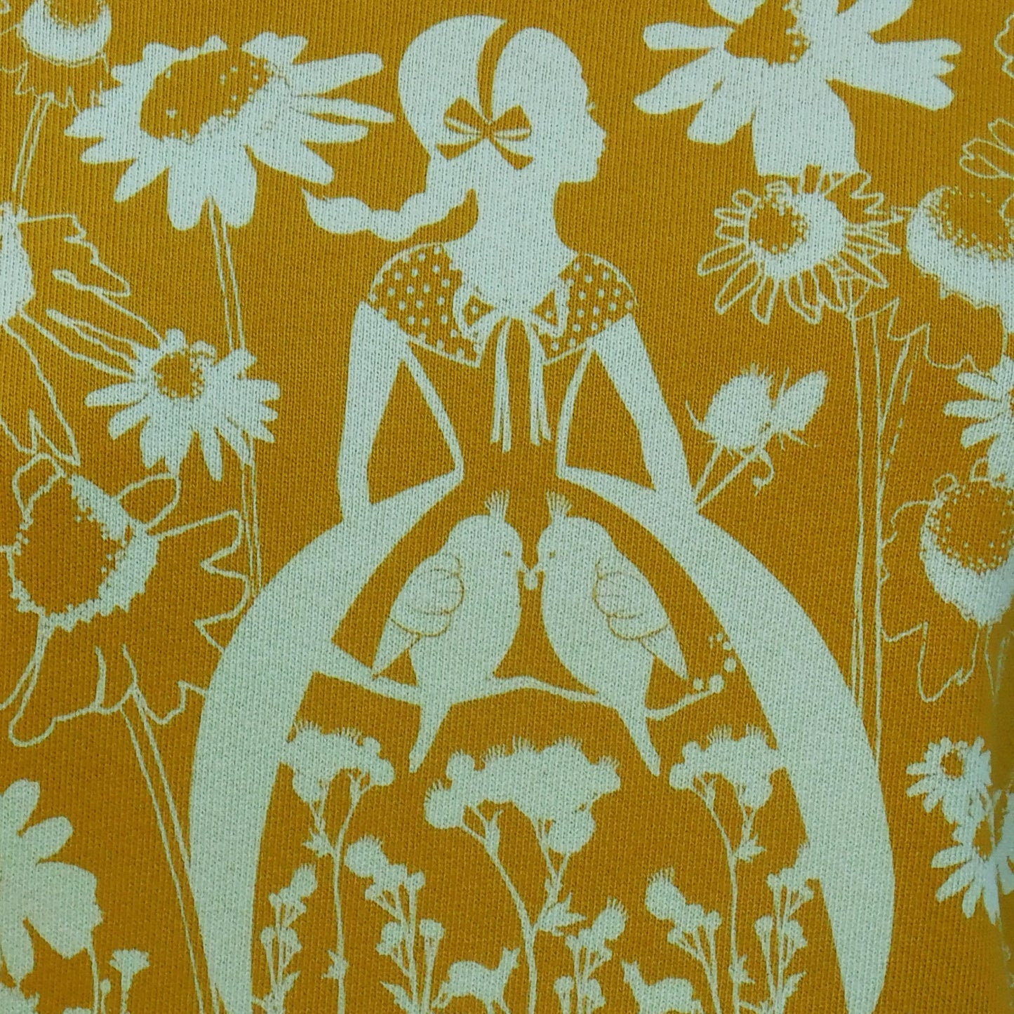 Closeup of screenprint of yellow shirt with white print of girl surrounded by daisies and birds