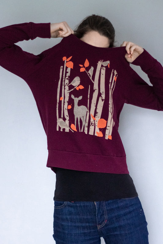 Model pulling purple birch tree and deer-printed sweatshirt over her head