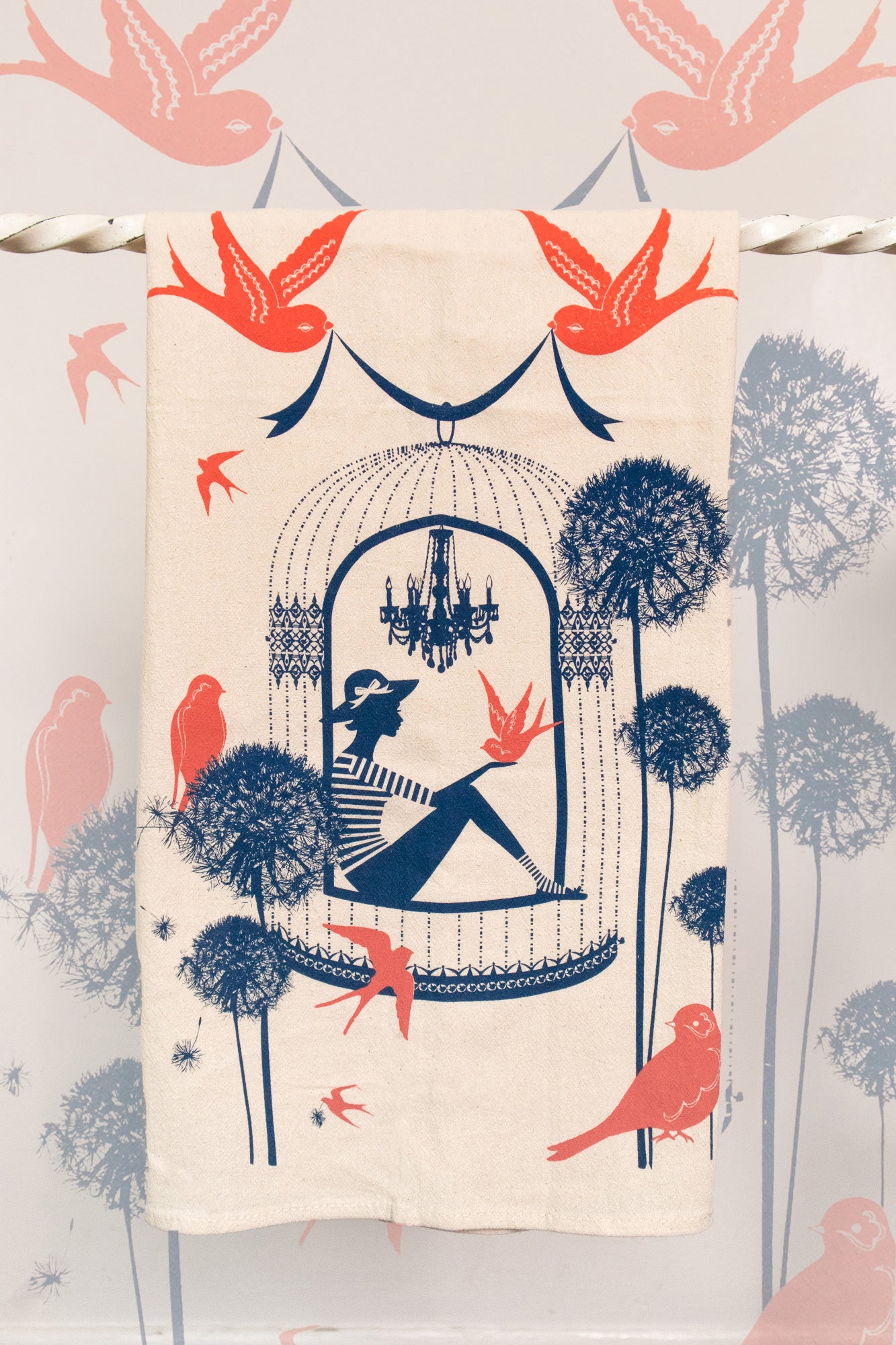 A colorful cotton tea towel with navy and coral print of birds and a woman in a birdcage