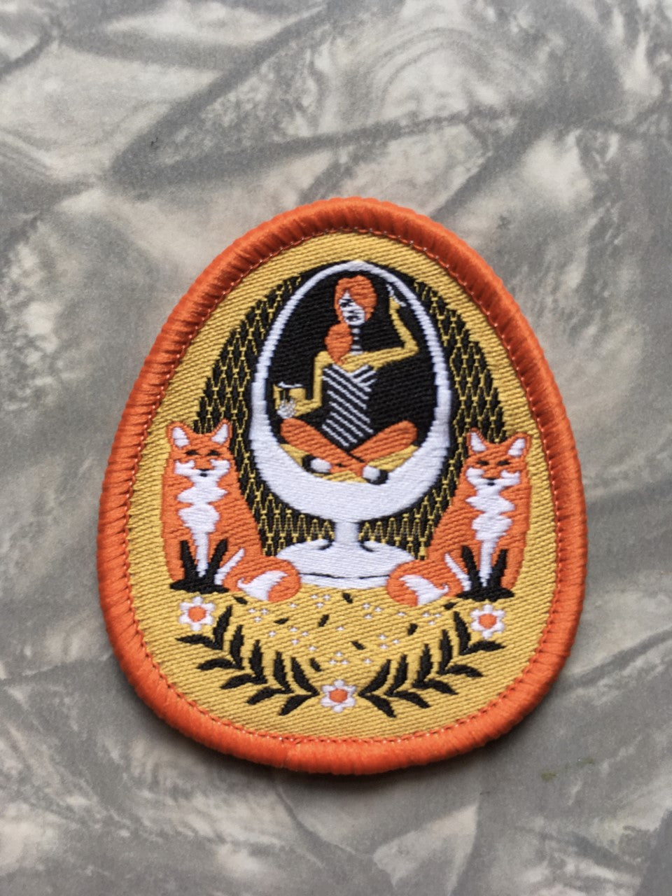 Yellow and orange iron-on patch featuring a girl in an egg chair with 2 foxes and flower accents