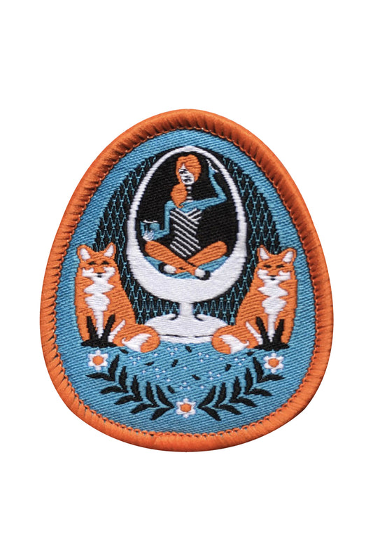 Sky blue and orange iron-on patch featuring a girl in an egg chair with 2 foxes and flower accents