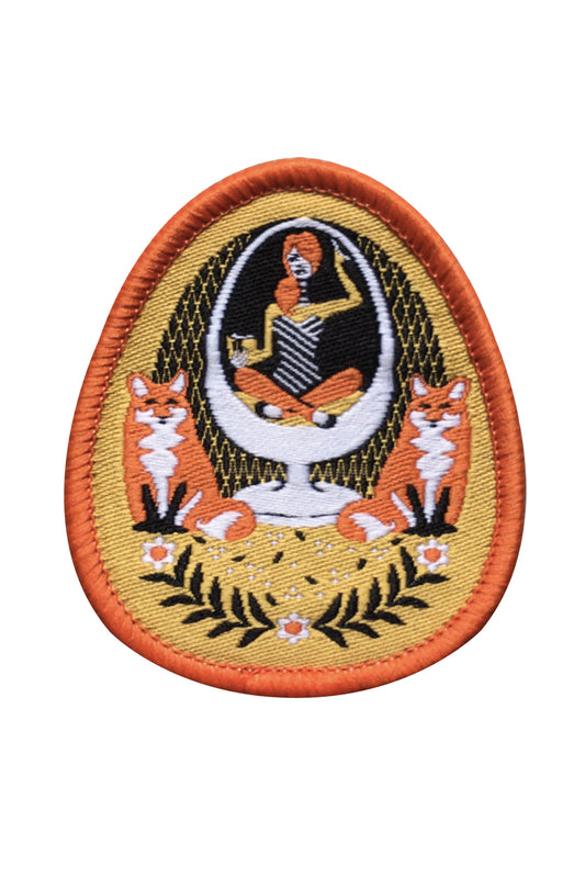 Yellow and orange iron-on patch featuring a girl in an egg chair with 2 foxes and flower accents