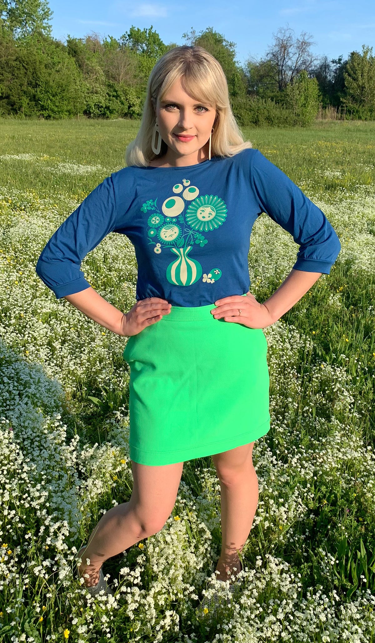 Cornflower blue boatneck tee with emerald green and white vintage vase of flowers design on pretty blonde model in a field of flowers