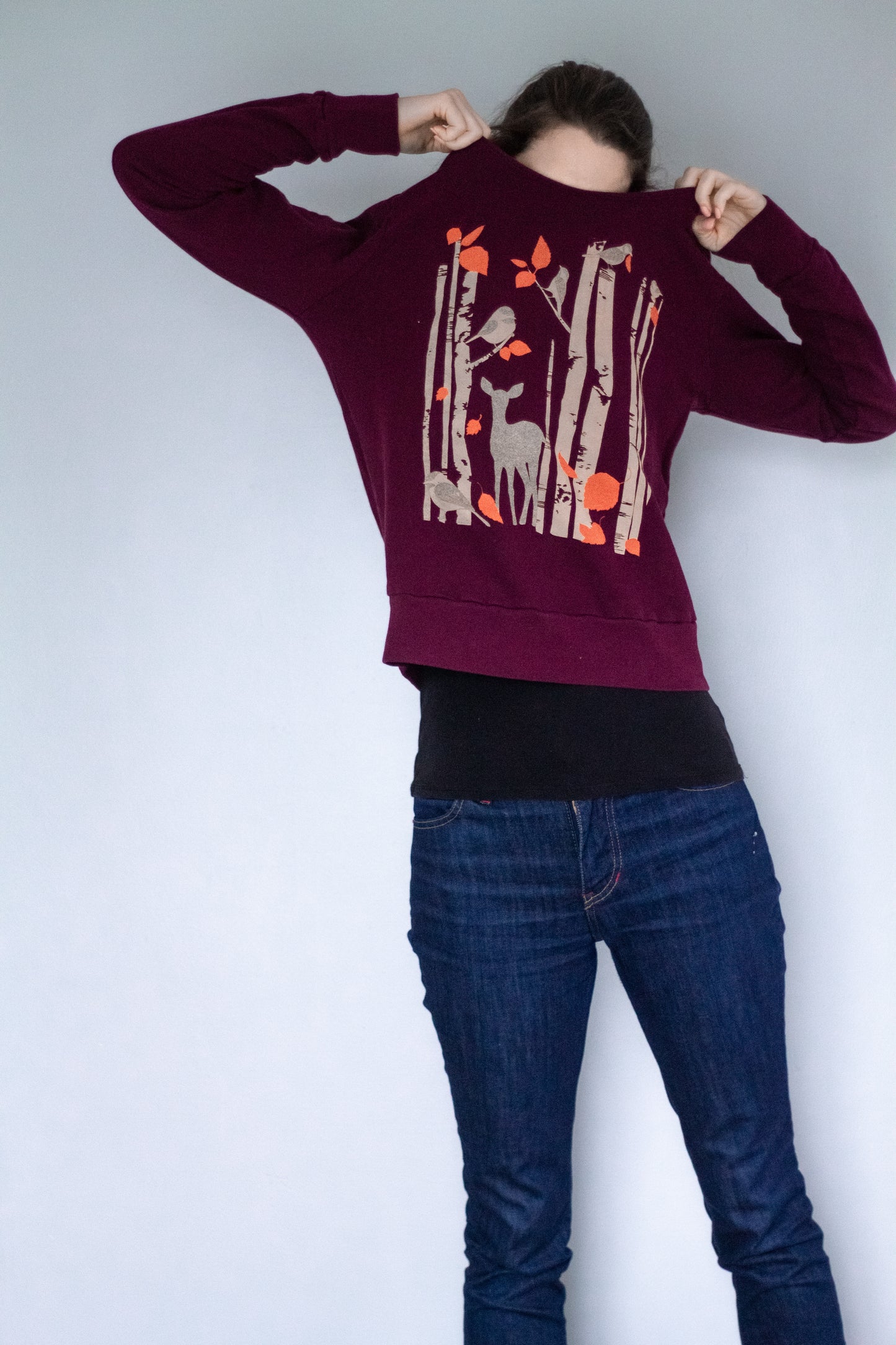 Model pulling purple birch tree and deer-printed sweatshirt over her head