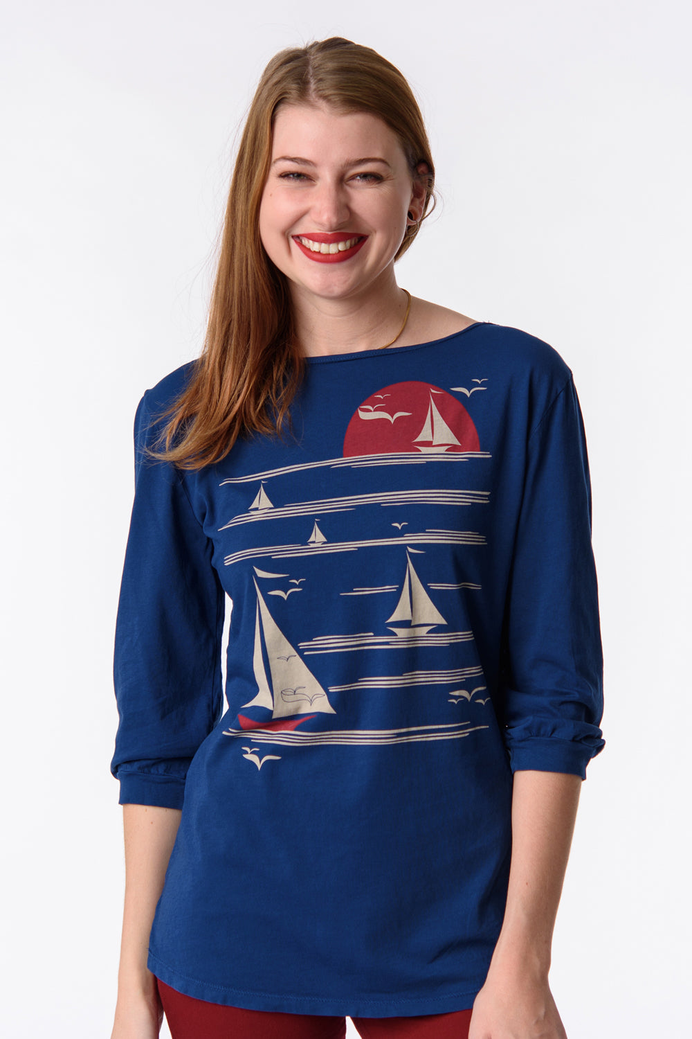 Blonde model wearing long sleeve blue shirt with graphic of boats on the water at sunset