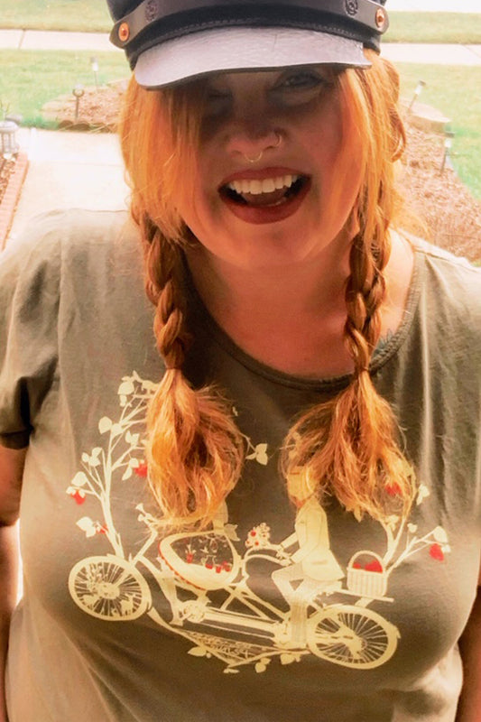Olive graphic tee with a couple riding tandem on redheaded woman with braids and a hat